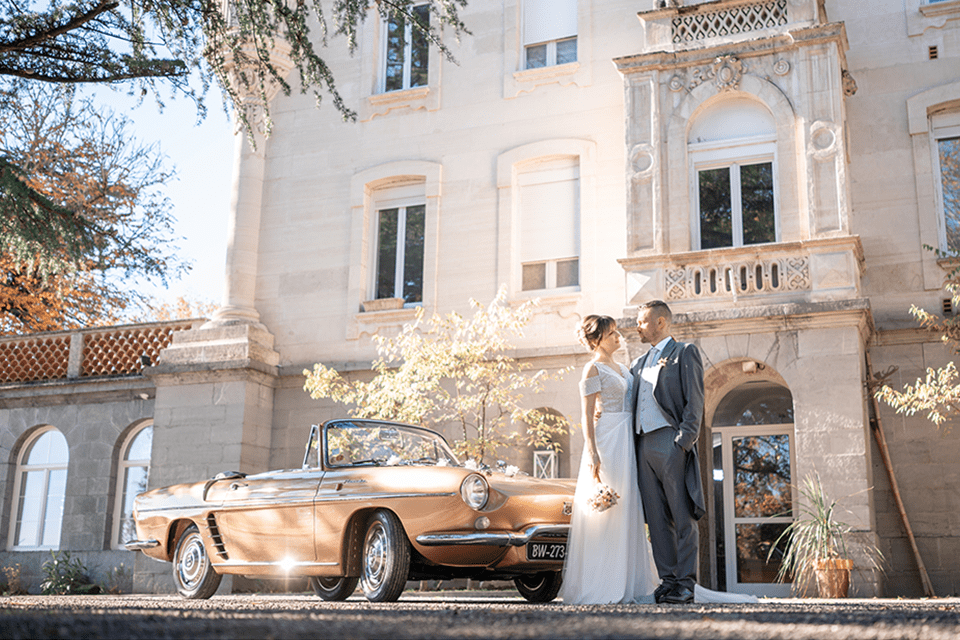 Couple de mariés à côté d’un château et d’une voiture de collection, ambiance sud