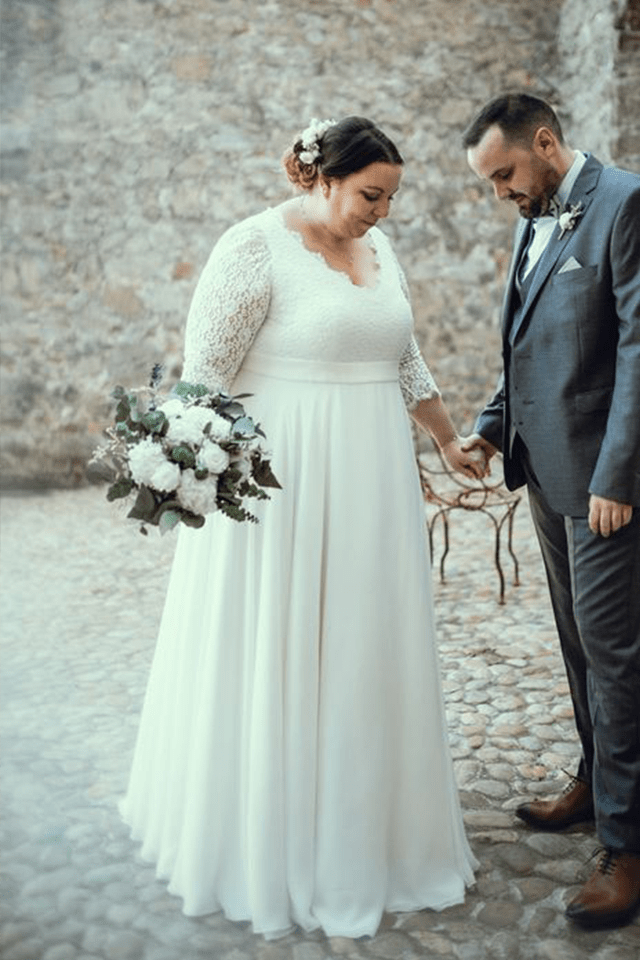 Femme ronde en robe de mariée tenant la main de son mari dans une cour pavée