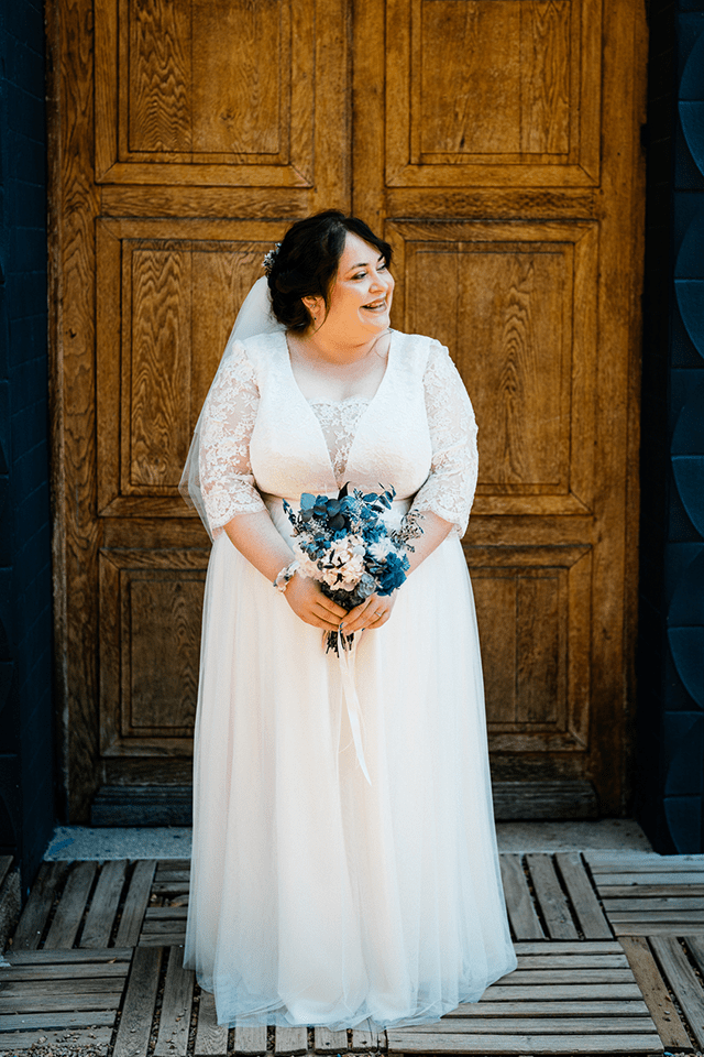 Mariée en robe grande taille souriante tenant un bouquet de fleurs