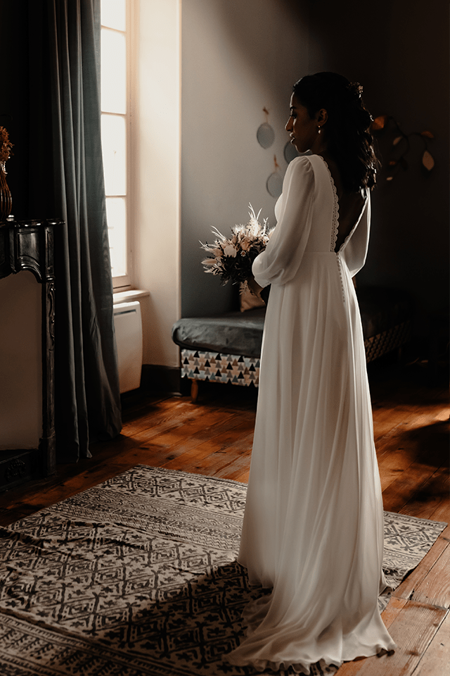 Mariée en robe dos nu longue dans un salon à l’ambiance tamisée