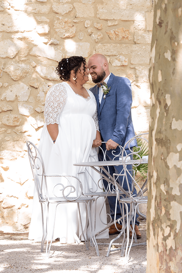 Mariée grande taille et son mari posant devant un mur en pierre provençal