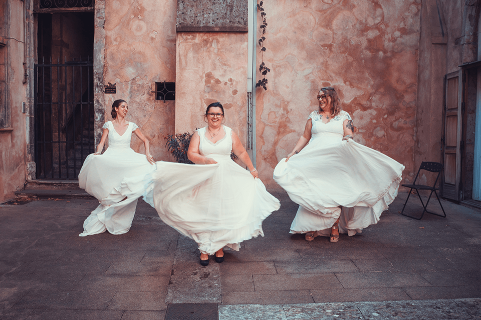 Trois femmes en robes de mariée dansant dans une cour extérieure