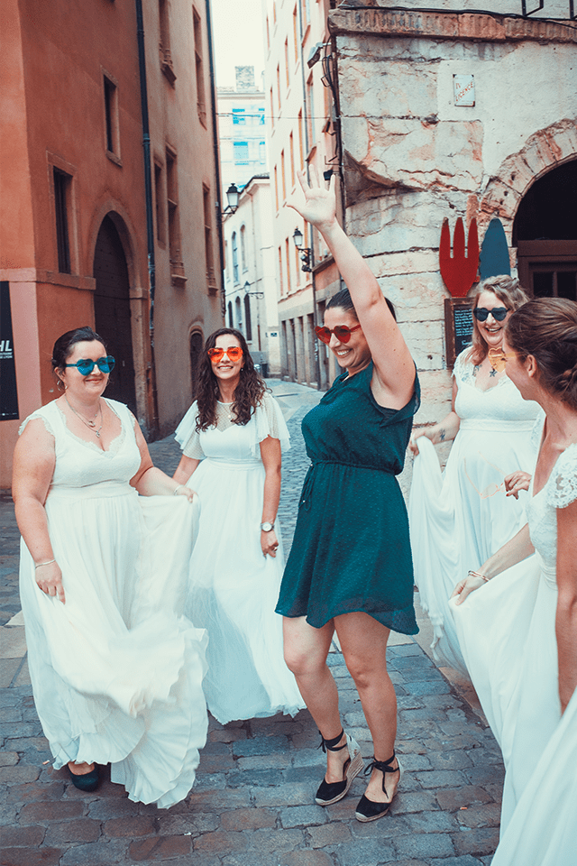 Karolle Anne dansant au milieu de femmes en robe de mariée dans une rue pavée