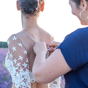 Fermeture de dernière minute d’une robe de mariée en dentelle lors d’un essayage en extérieur, dans un champ de lavande en Provence
