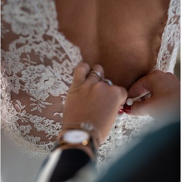 Main d'une femme refermant le dos d'une robe de mariee en dentelle transparente