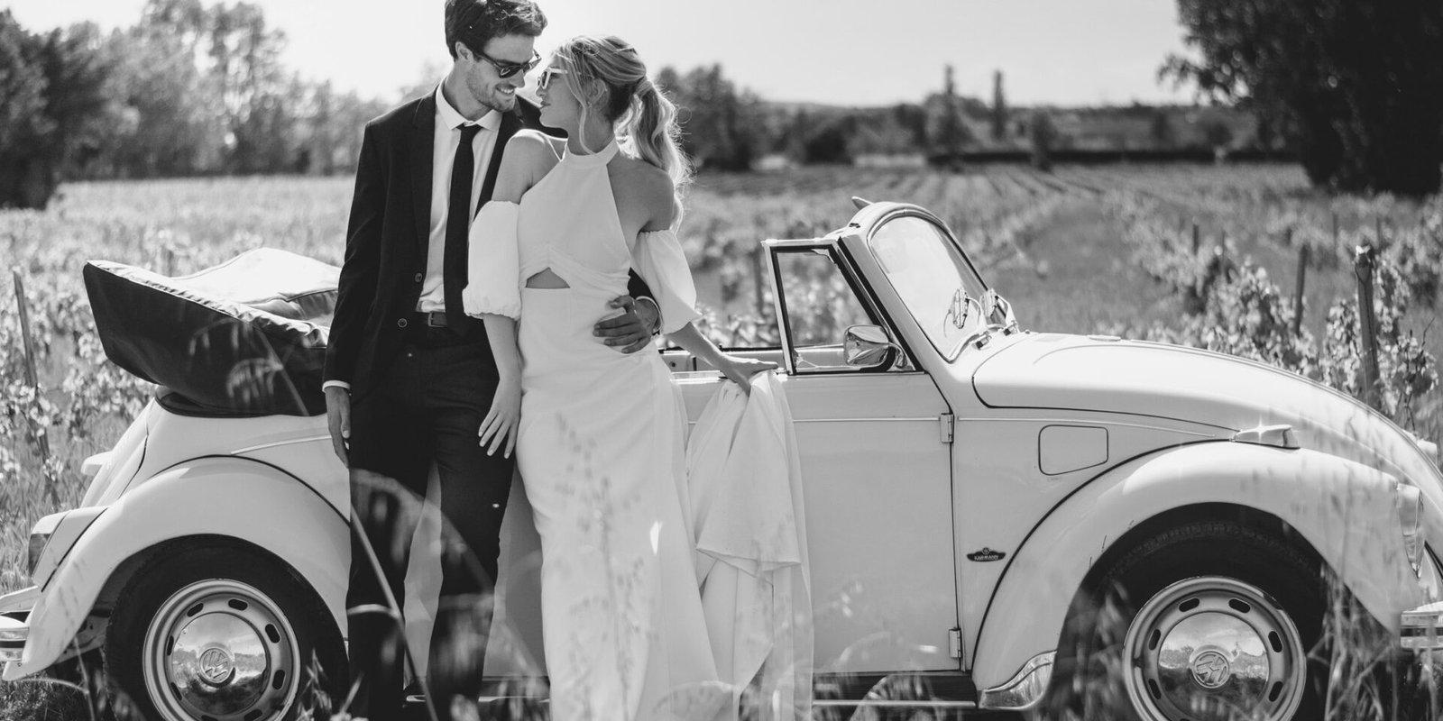 Couple de mariees adosses a une voiture vintage cabriolet